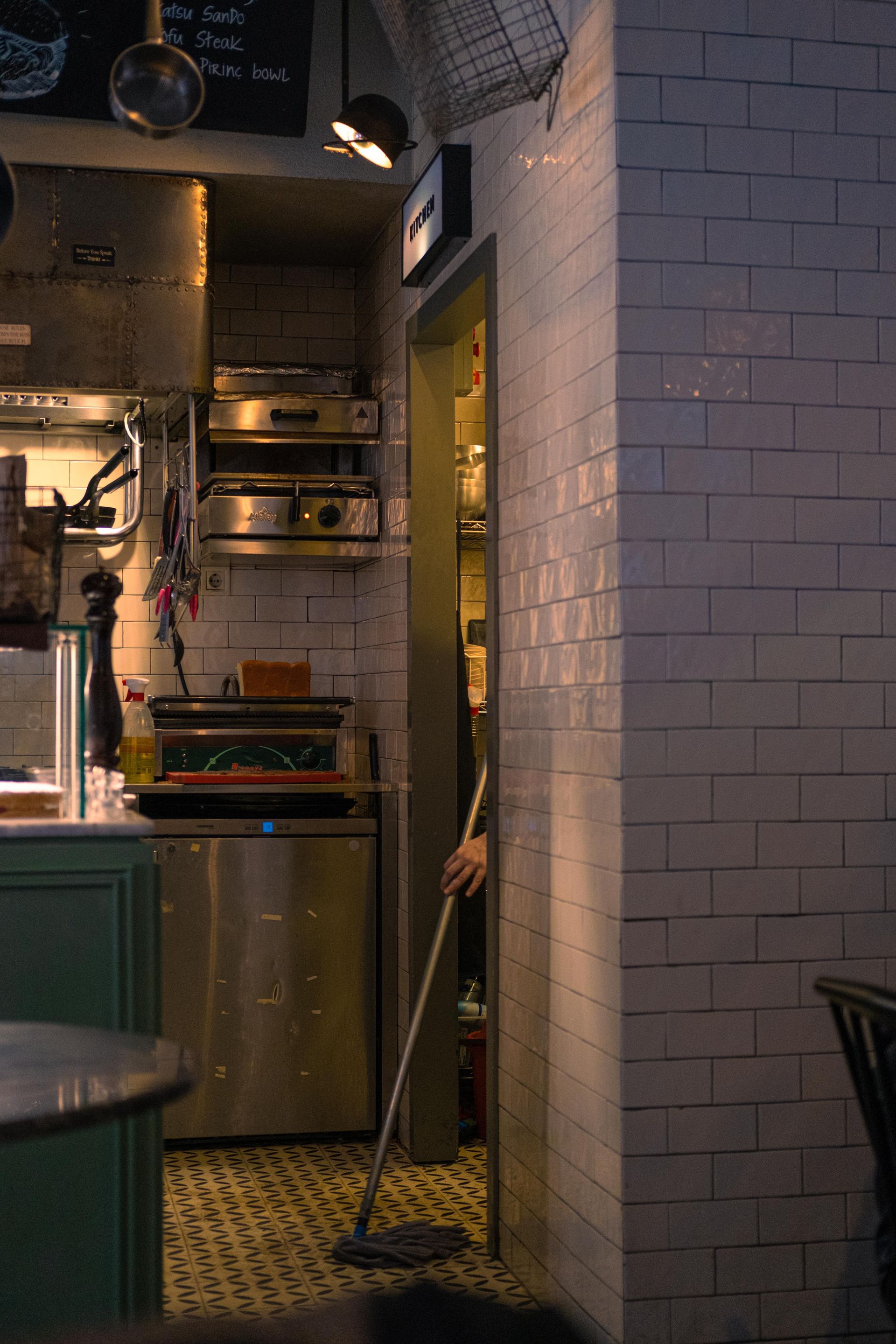 Warmly lit restaurant kitchen corner with subtle industrial decor and tiled walls.